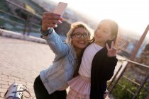 Jovem mãe feliz com sua filha tirando uma selfie na cidade em um dia ensolarado . — Fotografia de Stock