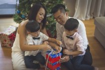 Mutter und Vater sitzen mit ihren beiden Söhnen zusammen auf dem Fußboden und bereiten ein paar Weihnachtsgeschenke für Freunde vor. — Stockfoto