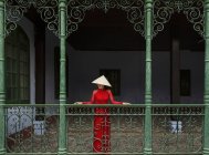 Vietnamesische Frau mit kegelförmigem Hut steht auf einem Balkon in hoi an in ihrem ao dai — Stockfoto