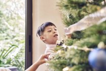 Little asian boy decorating christmas fir tree — Stock Photo
