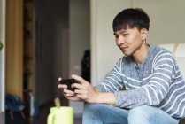 Jovem adulto asiático homem usando smartphone em casa — Fotografia de Stock