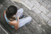 Молода азіатська спортивна жінка використовує смартфон на сходах — стокове фото