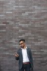 Homem de negócios indiano bonito usando smartphone contra parede de tijolo — Fotografia de Stock