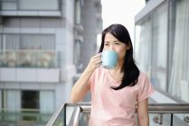Junge lässige asiatische Frau trinkt Tee auf Balkon — Stockfoto