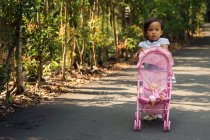 Cute little asian girl in park with baby carriage — Stock Photo