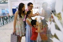 Giovane famiglia asiatica alla ricerca attraverso il vetro nel centro commerciale — Foto stock