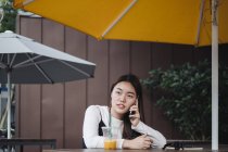 Hübsche Chinesin mit langen Haaren unterhält sich im Café am Smartphone — Stockfoto