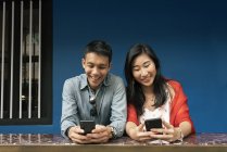Молодая счастливая азиатская пара с помощью смартфонов — стоковое фото