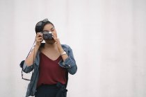 Молода приваблива азіатська жінка фотографується з камерою на білому тлі — стокове фото