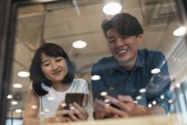 Two young asian people with smartphones in modern office — Stock Photo