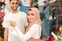 Jovem casal muçulmano na loja de flores, menina olhando para a direita na câmera, sorrindo — Fotografia de Stock
