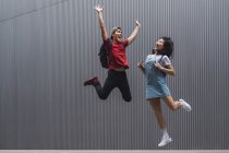 Giovani studenti universitari asiatici saltare e posa contro muro grigio — Foto stock