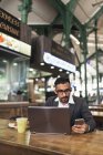 Bonito indiano homem de negócios usando laptop e comer no café — Fotografia de Stock