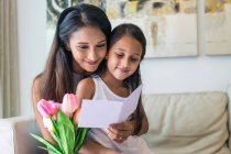 Joven asiático madre con lindo hija abrazo en casa con flores y plantilla - foto de stock