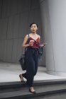 Молодая привлекательная азиатка пьет кофе и пользуется смартфоном на открытом воздухе — стоковое фото