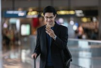 Exitoso asiático hombre de negocios usando smartphone en aeropuerto - foto de stock
