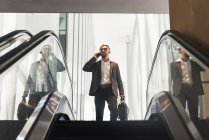 Schöner indischer Geschäftsmann spricht auf der Rolltreppe mit dem Smartphone — Stockfoto