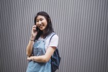 Молодий азіатський студент коледжу, використовуючи смартфон проти сірої стіни — стокове фото