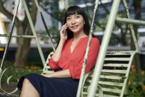 Молодая привлекательная азиатская бизнесвумен разговаривает на смартфоне на качелях — стоковое фото