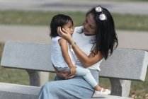 Mignonne adorable asiatique petite fille sur banc avec mère — Photo de stock
