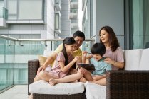 Счастливая молодая азиатская семья вместе с помощью цифрового планшета дома — стоковое фото