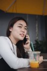 Hübsche Chinesin mit langen Haaren unterhält sich im Café am Smartphone — Stockfoto