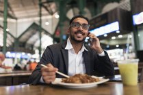 Красивий індійський бізнесмен використовує смартфон і їсть в кафе — стокове фото