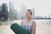 Young sporty asian woman with yoga mat at pier — Stock Photo