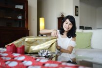 Joven asiático mujer envoltura navidad regalos en casa - foto de stock