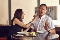 Young attractive asian couple having date in cafe, woman feeding man — Stock Photo
