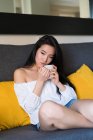 Giovane donna cinese su un divano a bere — Foto stock