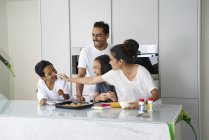 Giovane famiglia asiatica che celebra Hari Raya insieme a casa e cucina piatti tradizionali — Foto stock