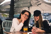 Две красивые подруги используют смартфон в кафе — стоковое фото