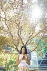 Schöne malaiische Frau im Park mit ihrem Handy — Stockfoto