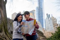 Felices turistas pareja sosteniendo mapa en el parque central - foto de stock