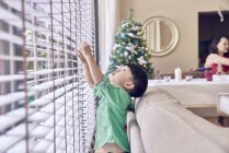 Feliz joven asiático chico mirando por la ventana en Navidad - foto de stock