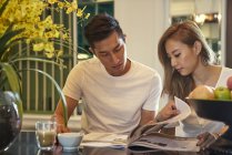 Happy young asian couple sitting together in cafe and reading magazine — Stock Photo
