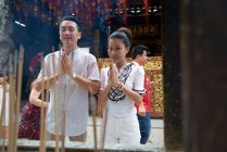 Young asian man and woman praying in temple with joss sticks — Stock Photo
