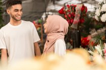 Joven pareja musulmana en floristería sonriéndose mutuamente - foto de stock