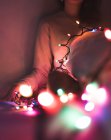 Abgeschnittenes Bild einer Frau, die es sich zu Hause mit Weihnachtsgirlanden gemütlich macht — Stockfoto