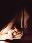 Menina bonito está lendo um livro na tenda — Fotografia de Stock