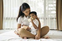 Asiatique mère montres comme son fils se nourrit sur lait bouteille — Photo de stock
