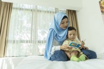 Giovane asiatica musulmana madre e bambino reding libro a casa — Foto stock