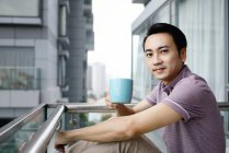 Дорослий азіатський чоловік має каву на балконі — стокове фото