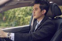 Jovem empresário motorista em um carro de condução de terno preto — Fotografia de Stock