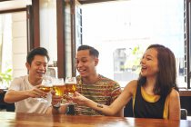Happy young asian friends drinking beer in bar — Stock Photo