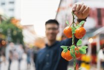 Jovem asiático homem mostrando tangerinas para câmera — Fotografia de Stock