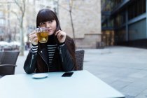 Jeune attrayant asiatique femme ayant thé dans la rue café — Photo de stock