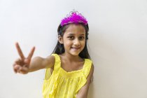 Молода маленька мила азіатська дівчинка в короні демонструє мирний жест — стокове фото