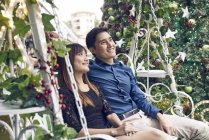 Happy young asian couple riding swing near fir tree — Stock Photo
